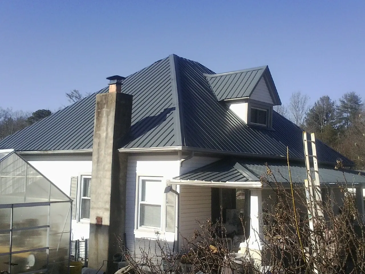 Dark blue standing seam metal roof on a white farmhouse with dormer — Slate & Tile Roof Repair by Roofing Brothers in Holly Hill