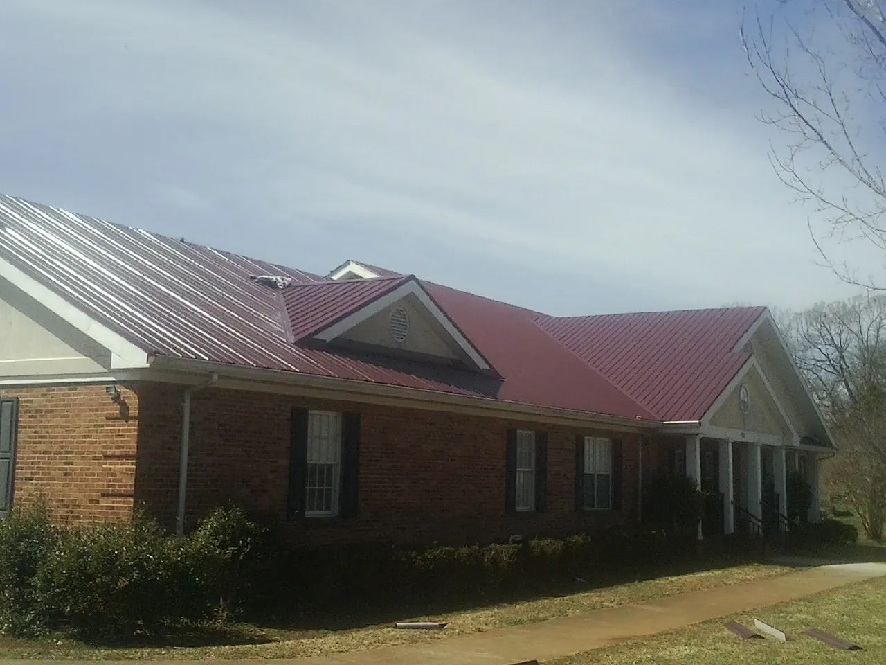 Red metal roof with gabled entries on a long brick building, from a Hail Damage Roof Repair job in Holly Hill