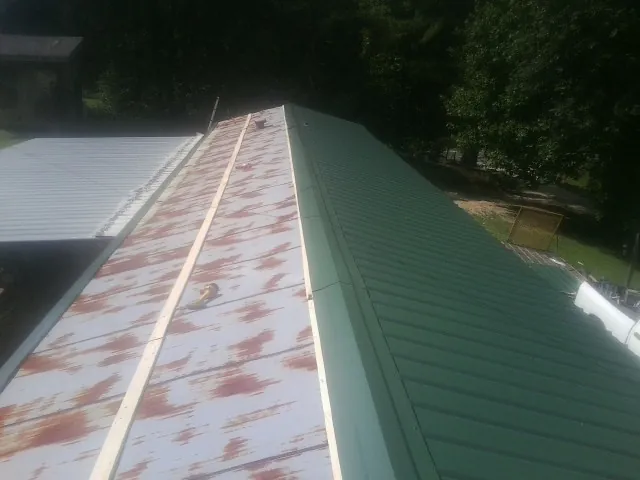 Old rusted panels beside newly installed green metal roofing — Wind Damage Roof Repair by Roofing Brothers in Holly Hill