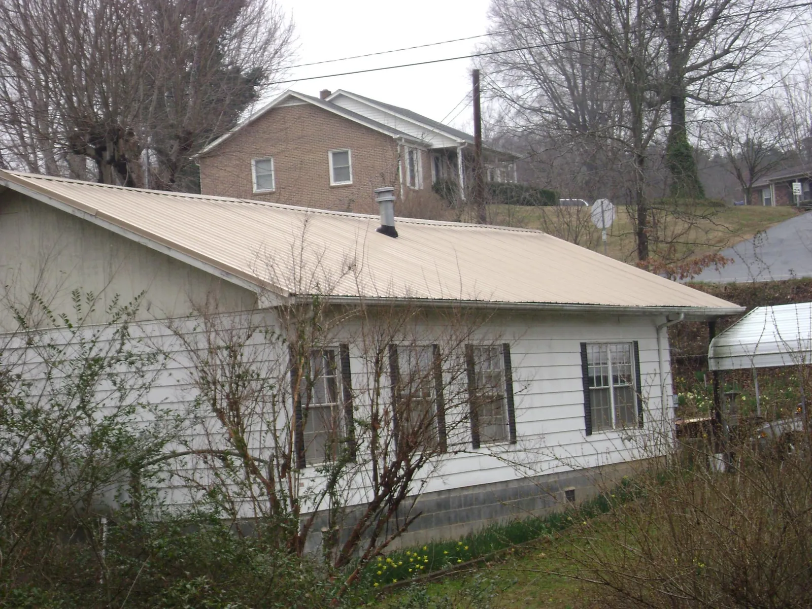 Tan metal roof on a white sided house set into a hillside — Commercial Roofing by Roofing Brothers in Holly Hill