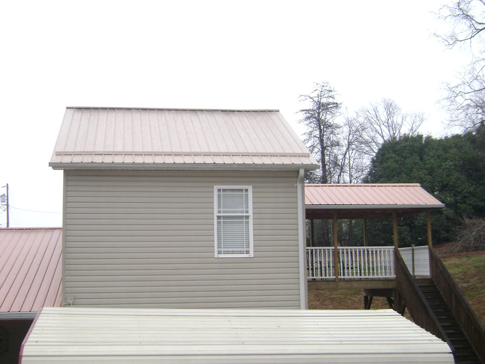 Tan metal roofs on a two story addition and attached porch, from a Roof Replacement job in Holly Hill